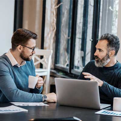 Men sitting at a table with a laptop and coffee - Assessing Your Business's Current State