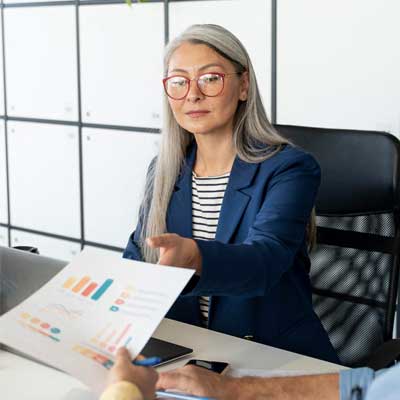 A woman in a blue jacket and red glasses pointing at a piece of paper - Assembling Your Transition Team